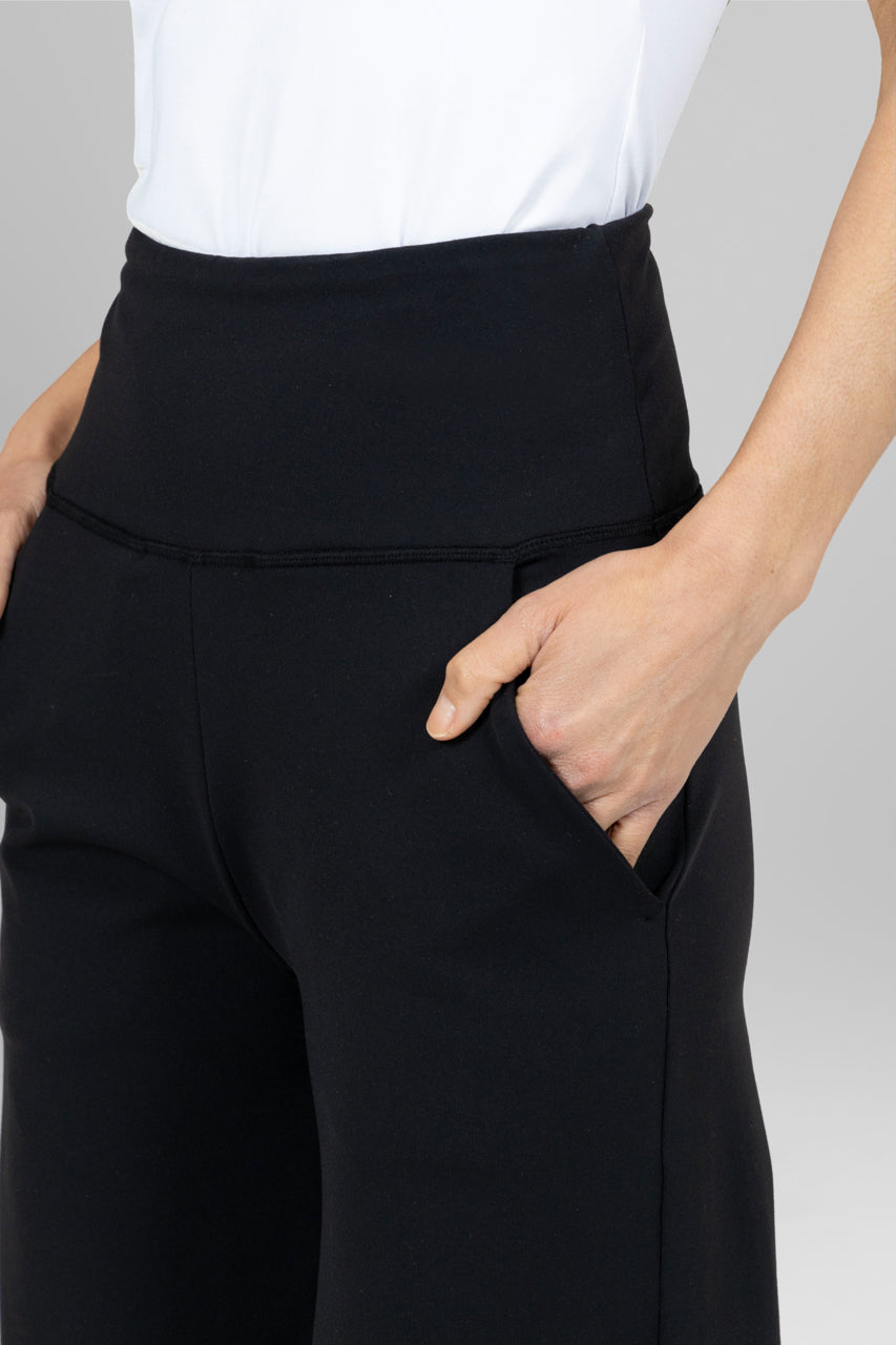 Person wearing black pants with a white top on a plain background