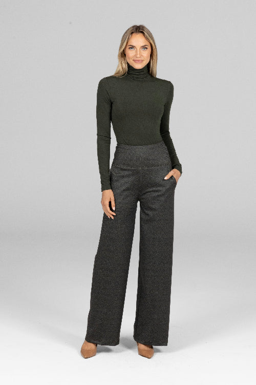 Woman wearing a green turtleneck and gray high-waisted pants on a white background