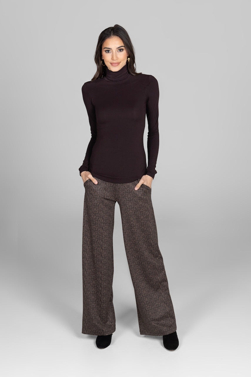 Woman wearing a dark brown turtleneck and wide-leg pants on a gray background
