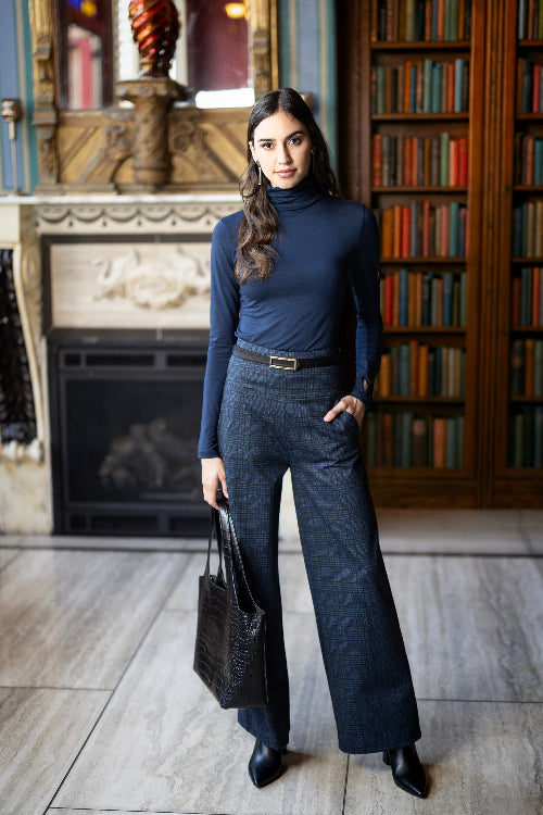 Woman in a blue outfit standing in a room with a fireplace and bookshelves.