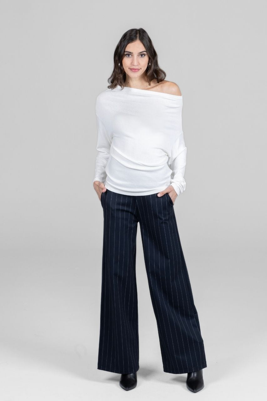 Woman wearing a white off-shoulder top and black pinstripe pants on a gray background