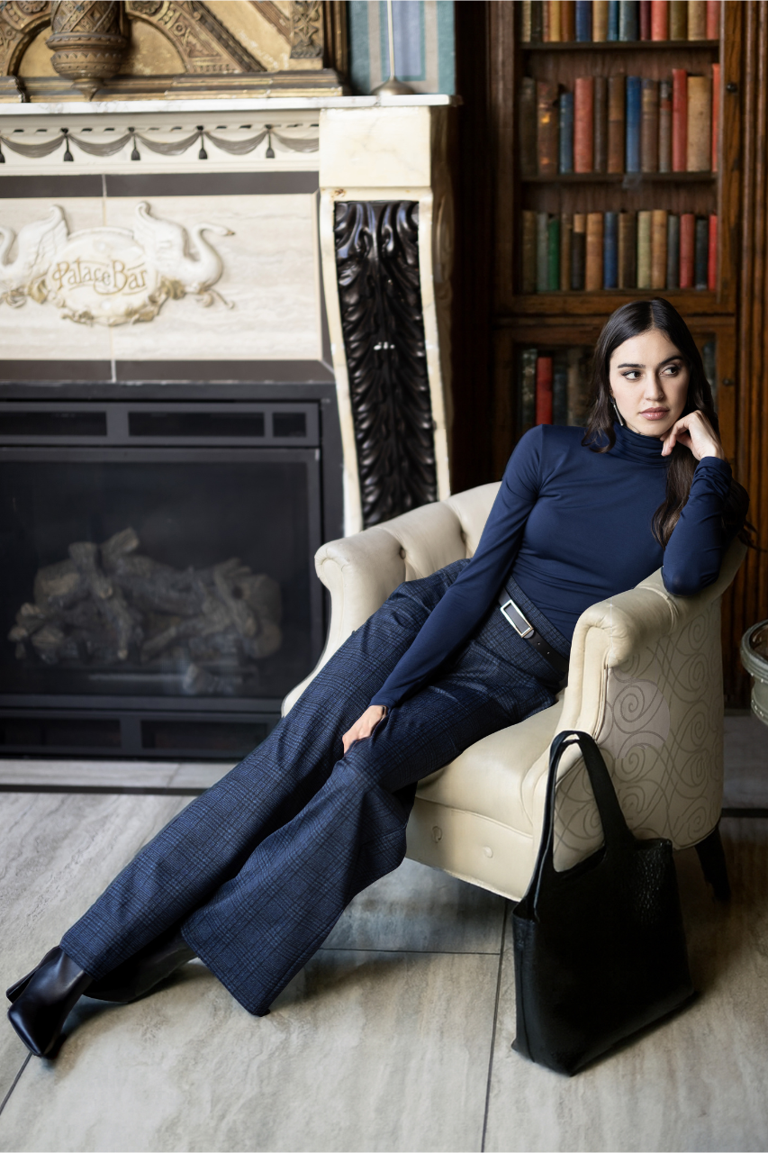 Woman in a blue outfit sitting on a chair in a room with a fireplace and bookshelf.