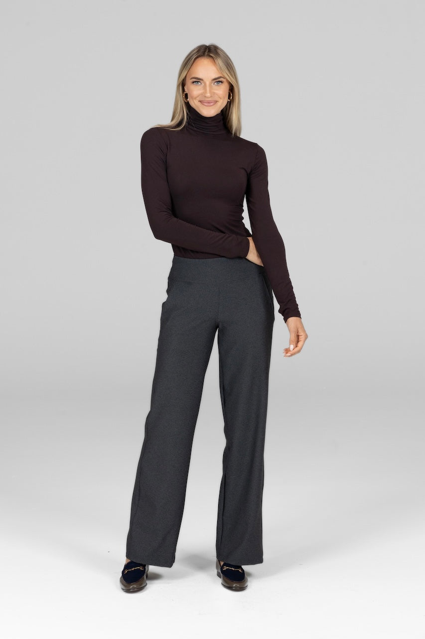 Woman wearing a brown turtleneck and gray pants on a white background