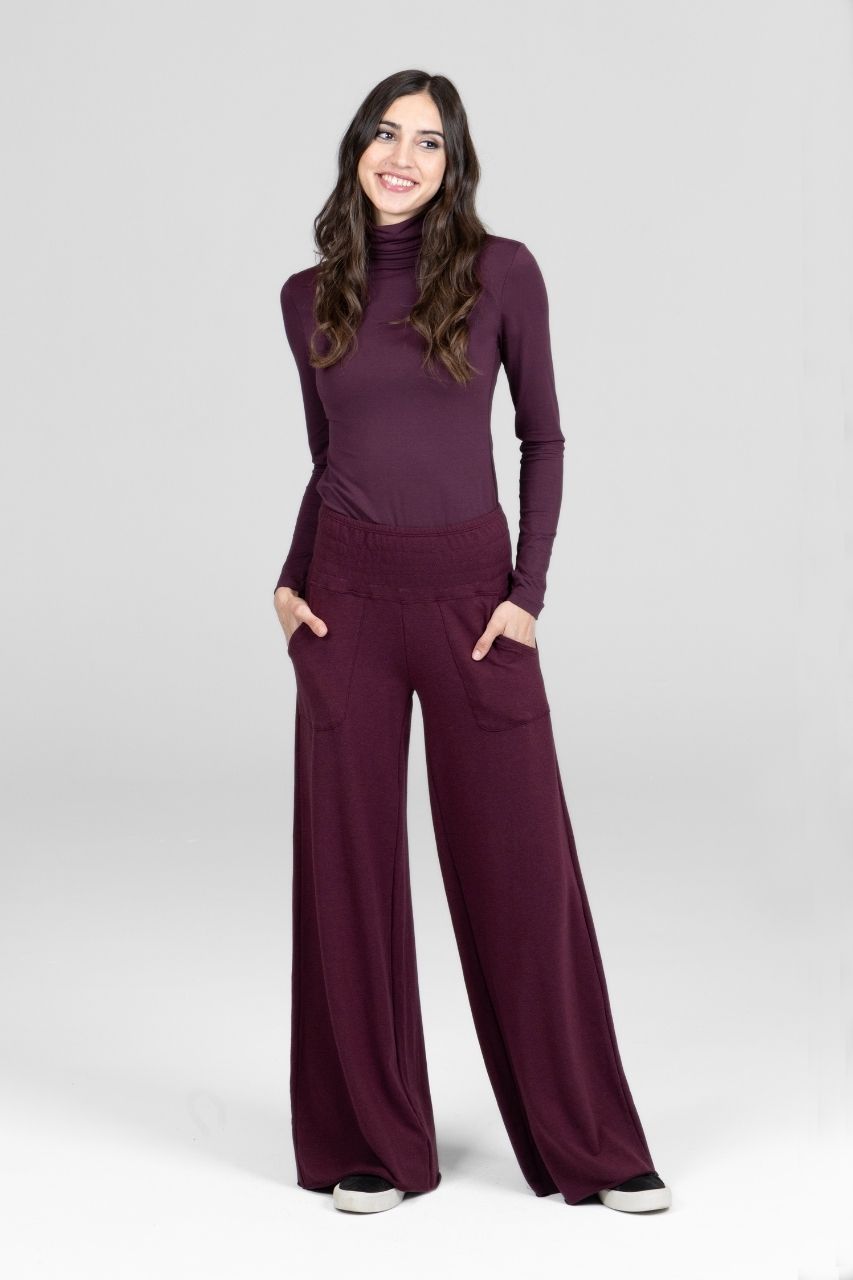 Woman wearing a purple outfit with a turtleneck and wide-leg pants on a white background