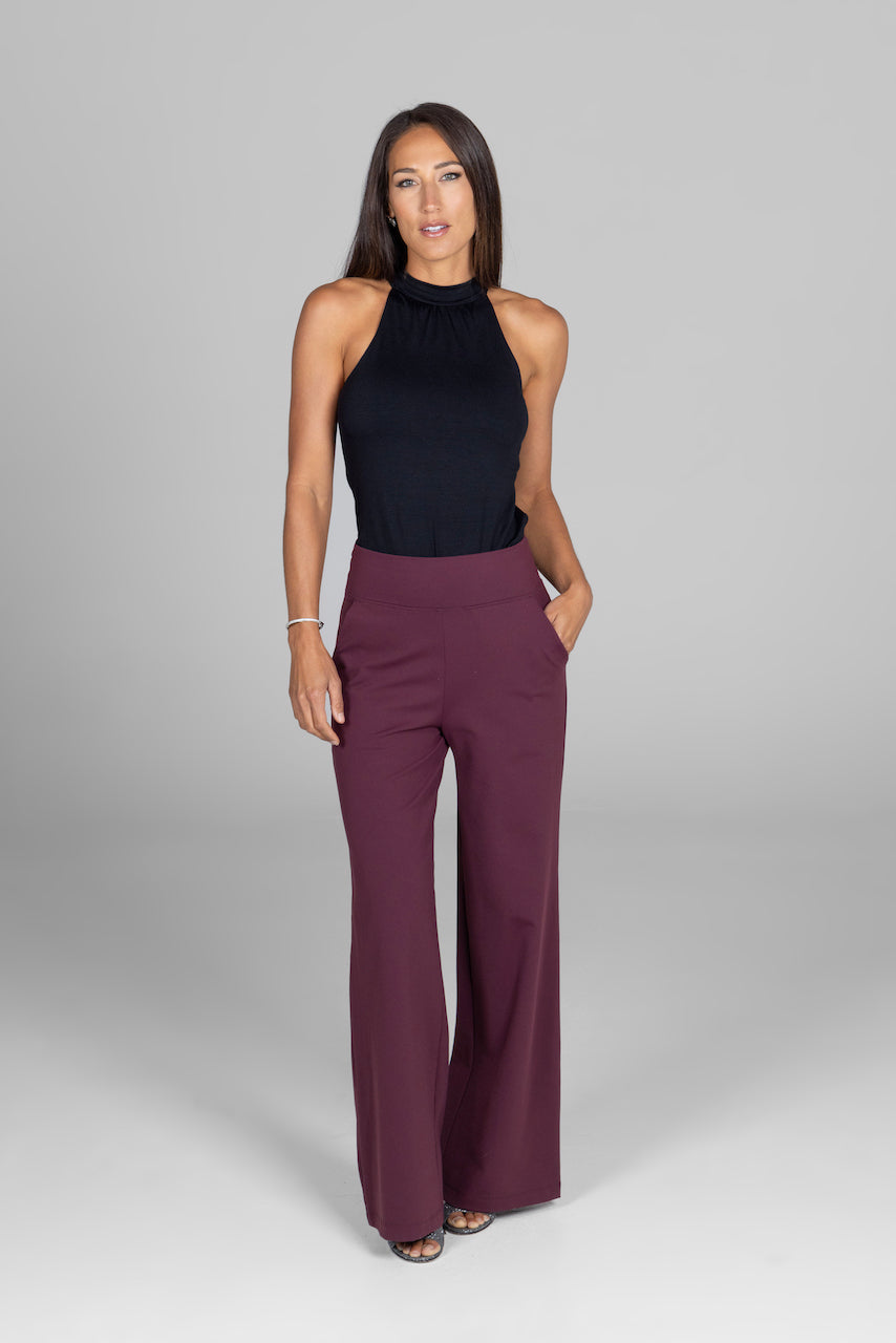 Woman wearing a black sleeveless top and maroon high-waisted pants on a gray background