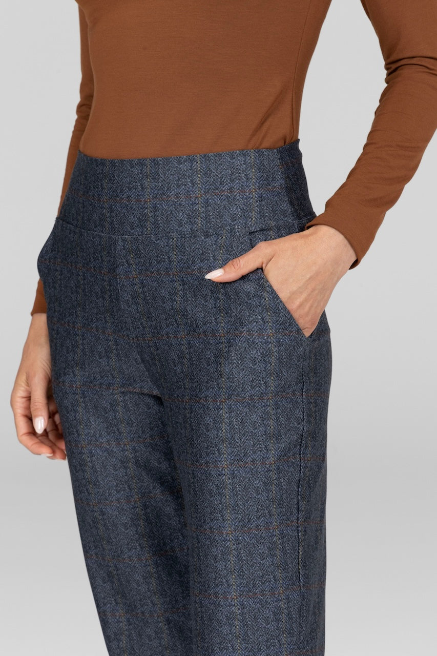 Person wearing a brown long-sleeve top and blue plaid pants on a light gray background