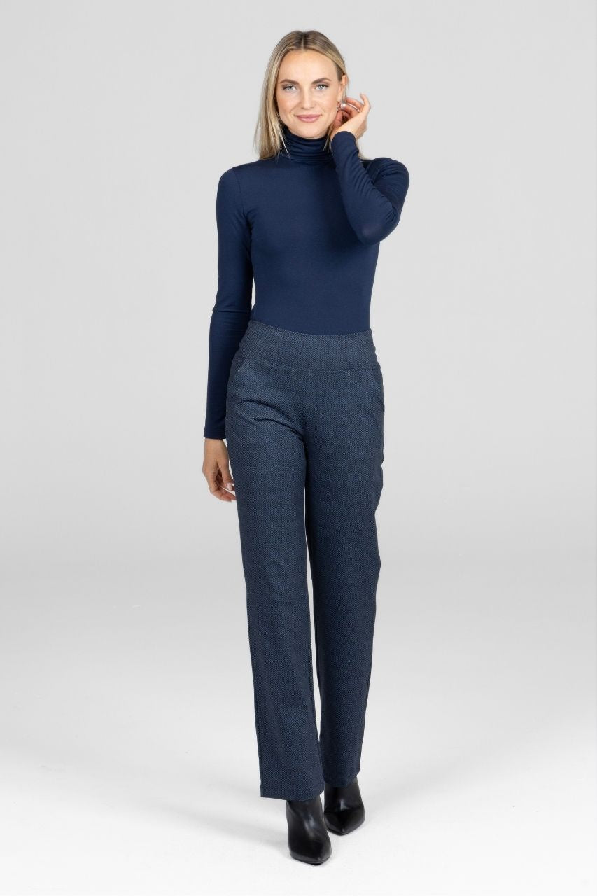Woman wearing a navy turtleneck and pants on a light gray background
