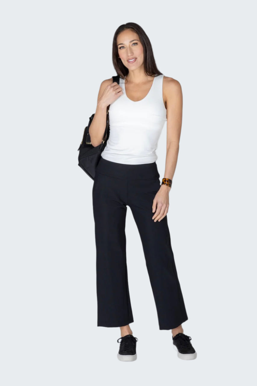 Woman wearing a white tank top and black pants on a plain background