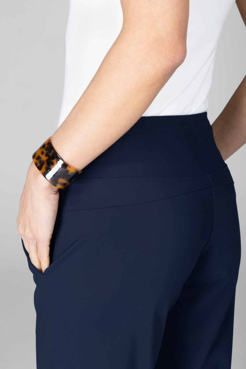 Navy blue pants worn by a person with a white shirt and leopard print bracelet on a gray background