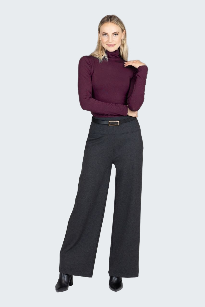 Woman wearing a purple turtleneck and black wide-leg pants on a white background