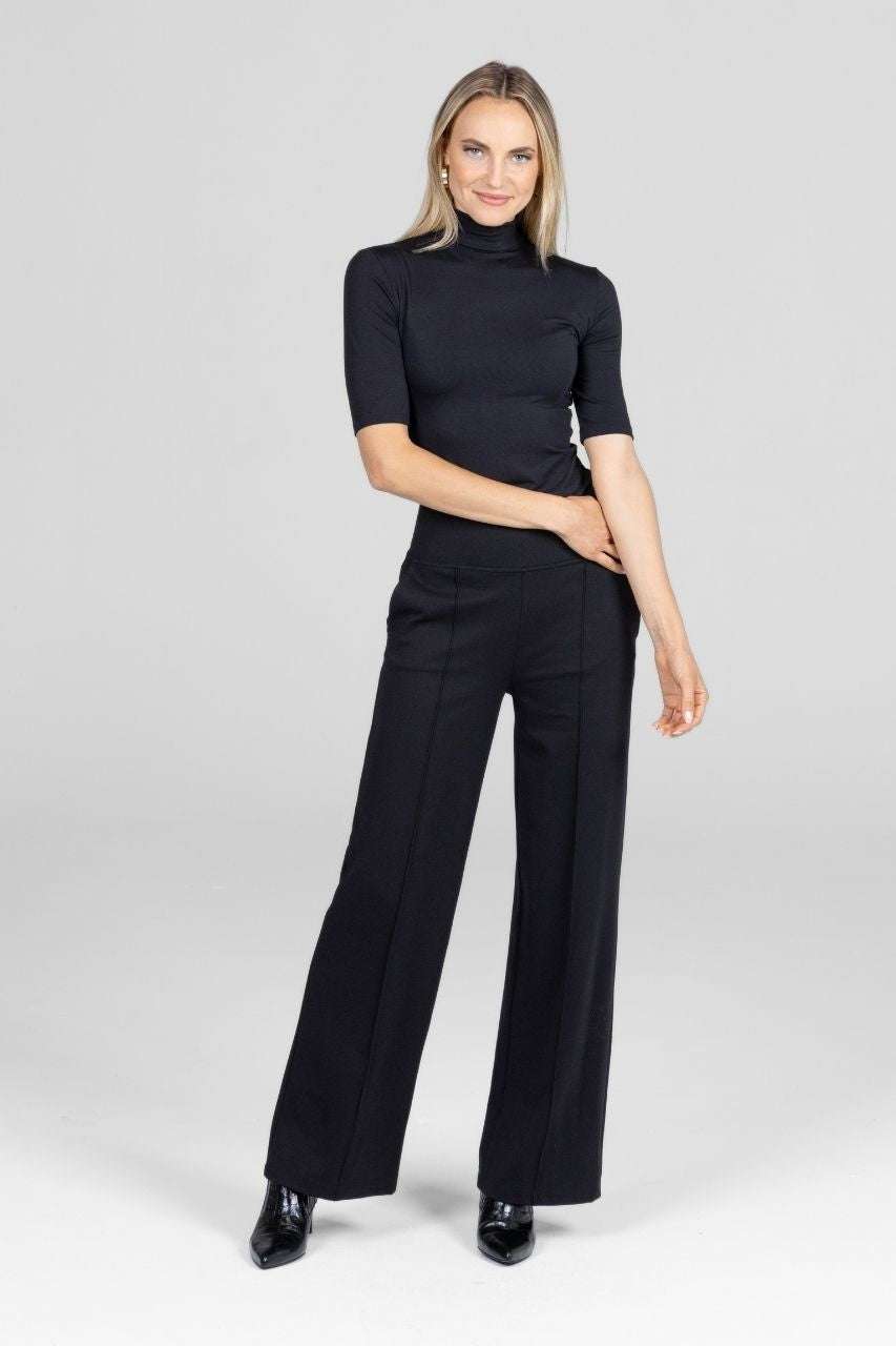 Woman wearing a black outfit with a turtleneck and wide-leg pants on a white background