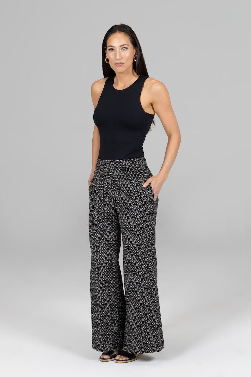 Woman wearing a black sleeveless top and patterned pants on a gray background
