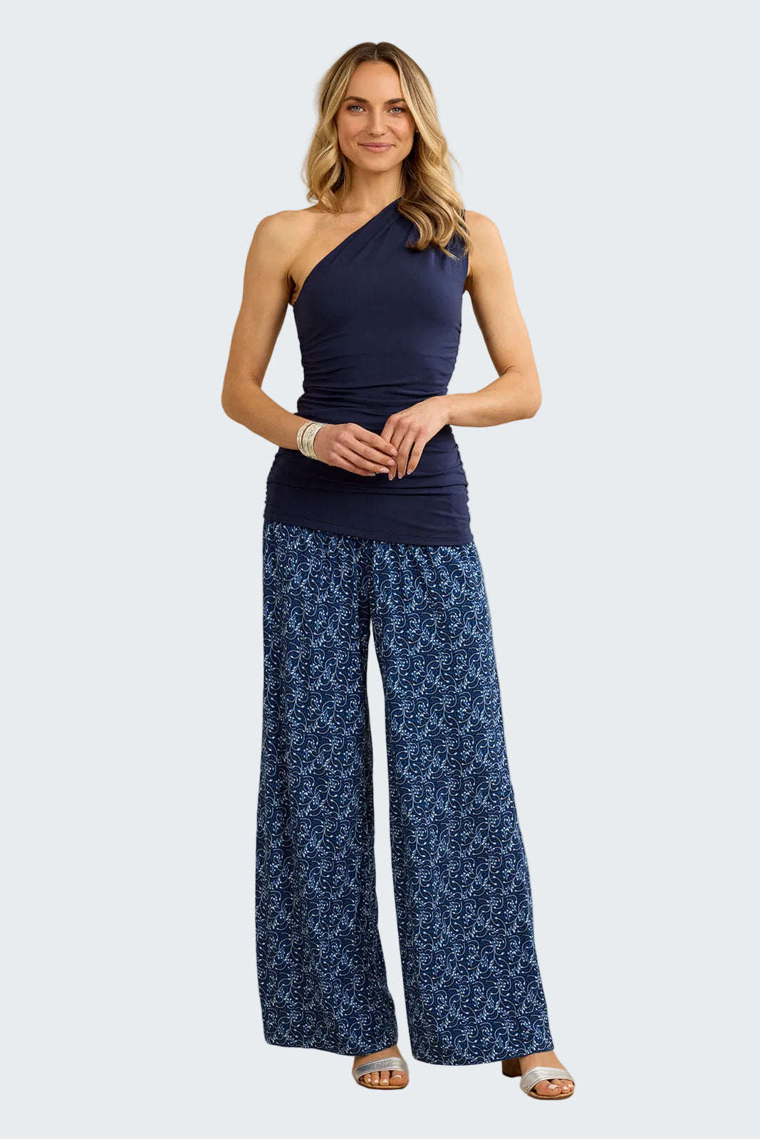 Woman wearing a navy one-shoulder top and blue patterned pants against a beige background