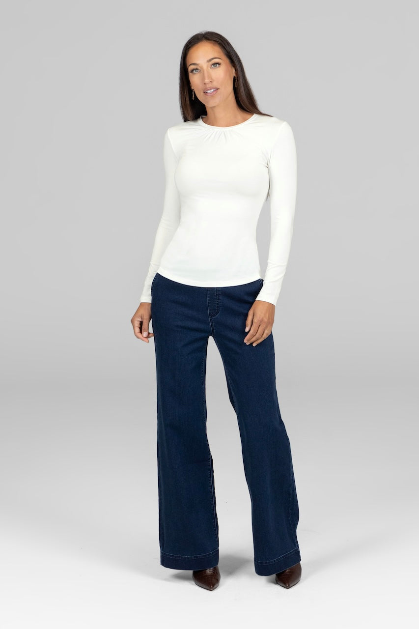 Woman wearing a white long-sleeve top and dark blue jeans on a gray background