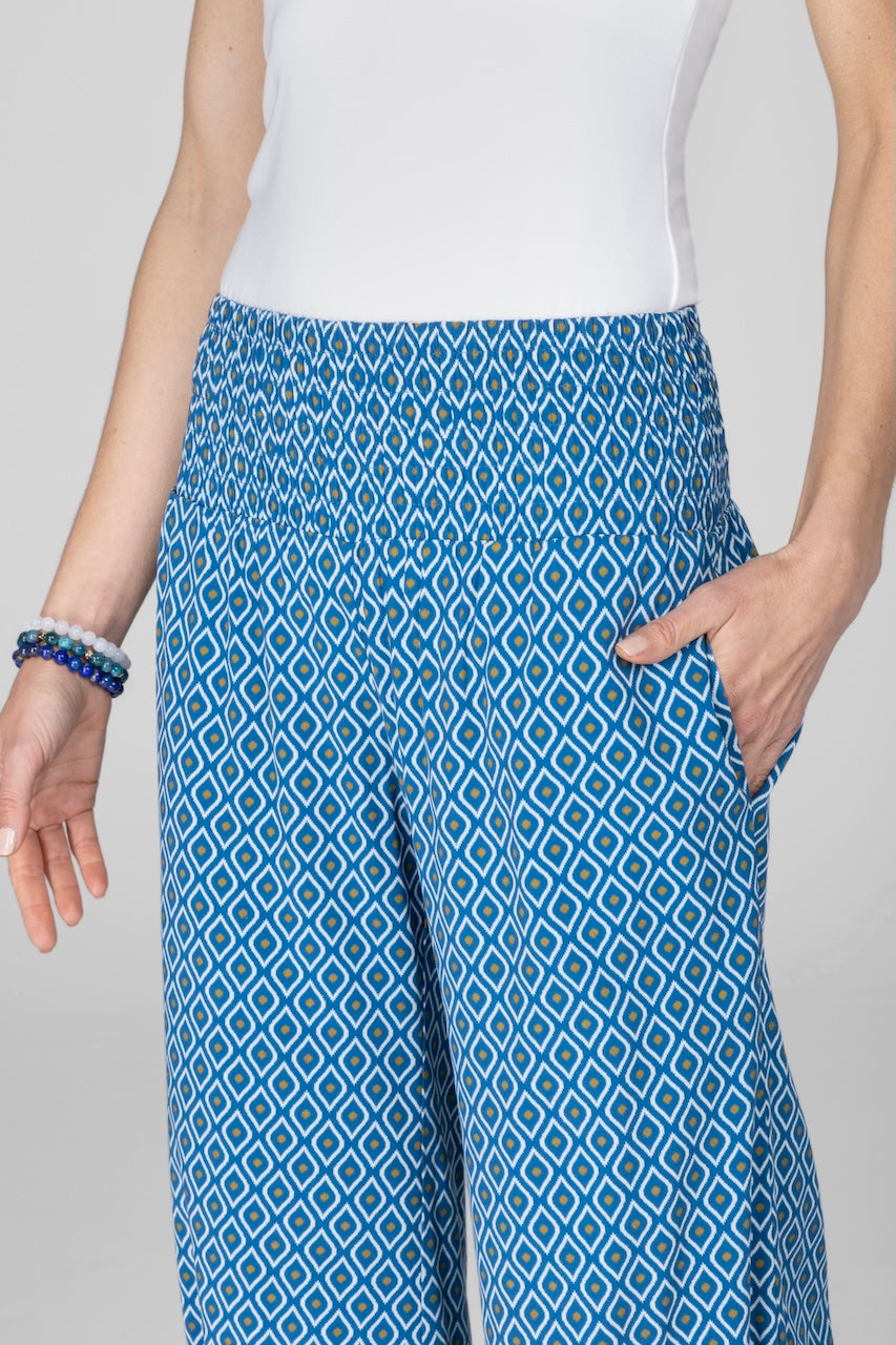 Person wearing blue patterned pants with a white top on a gray background