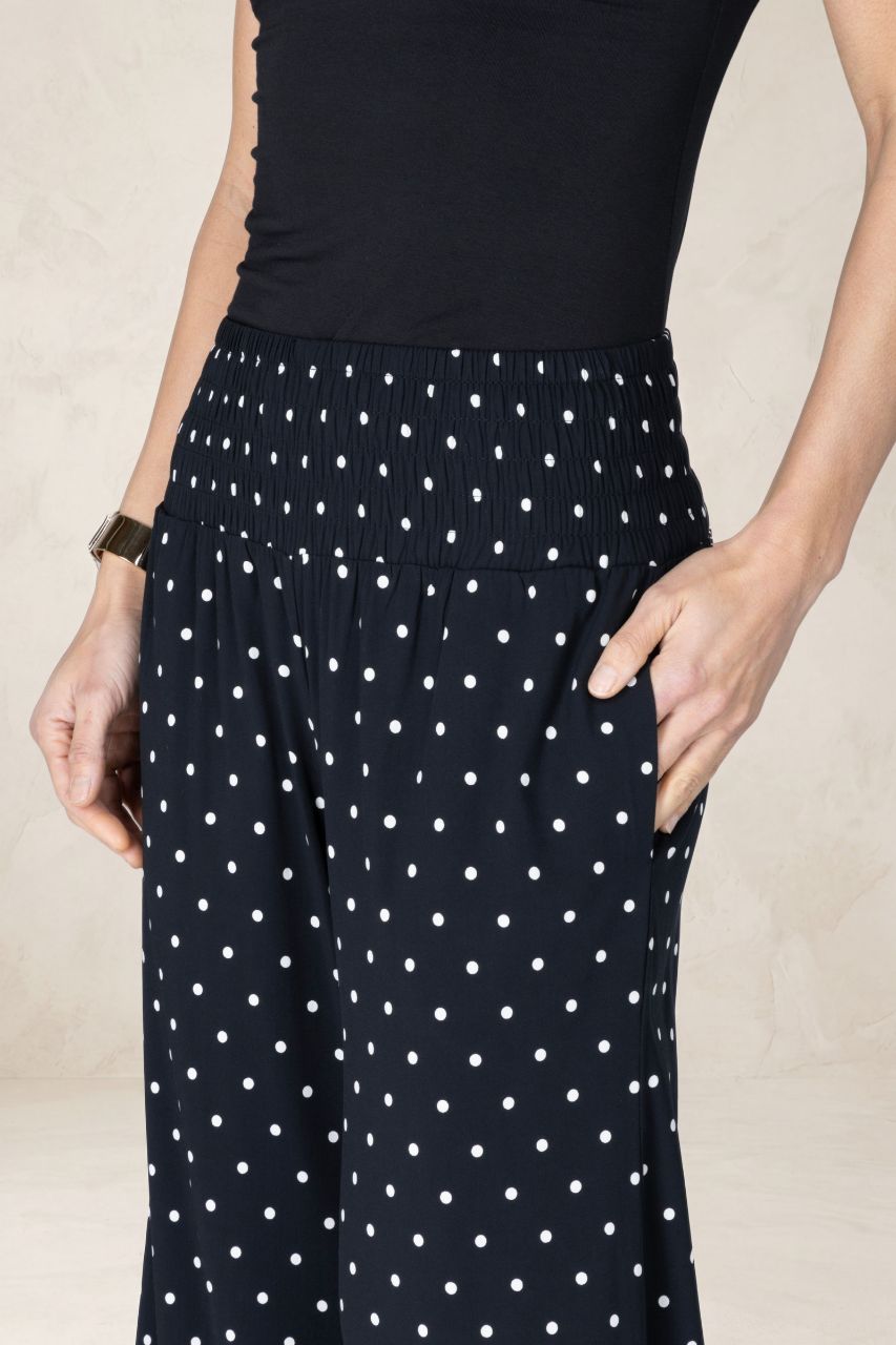 Navy blue pants with white polka dots worn by a person on a beige background