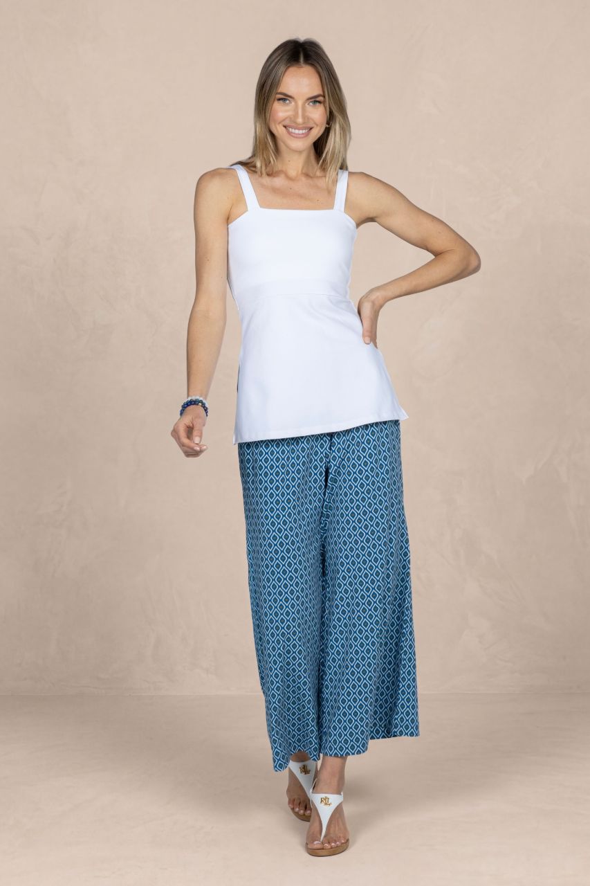 Woman wearing a white tank top and blue patterned pants on a beige background