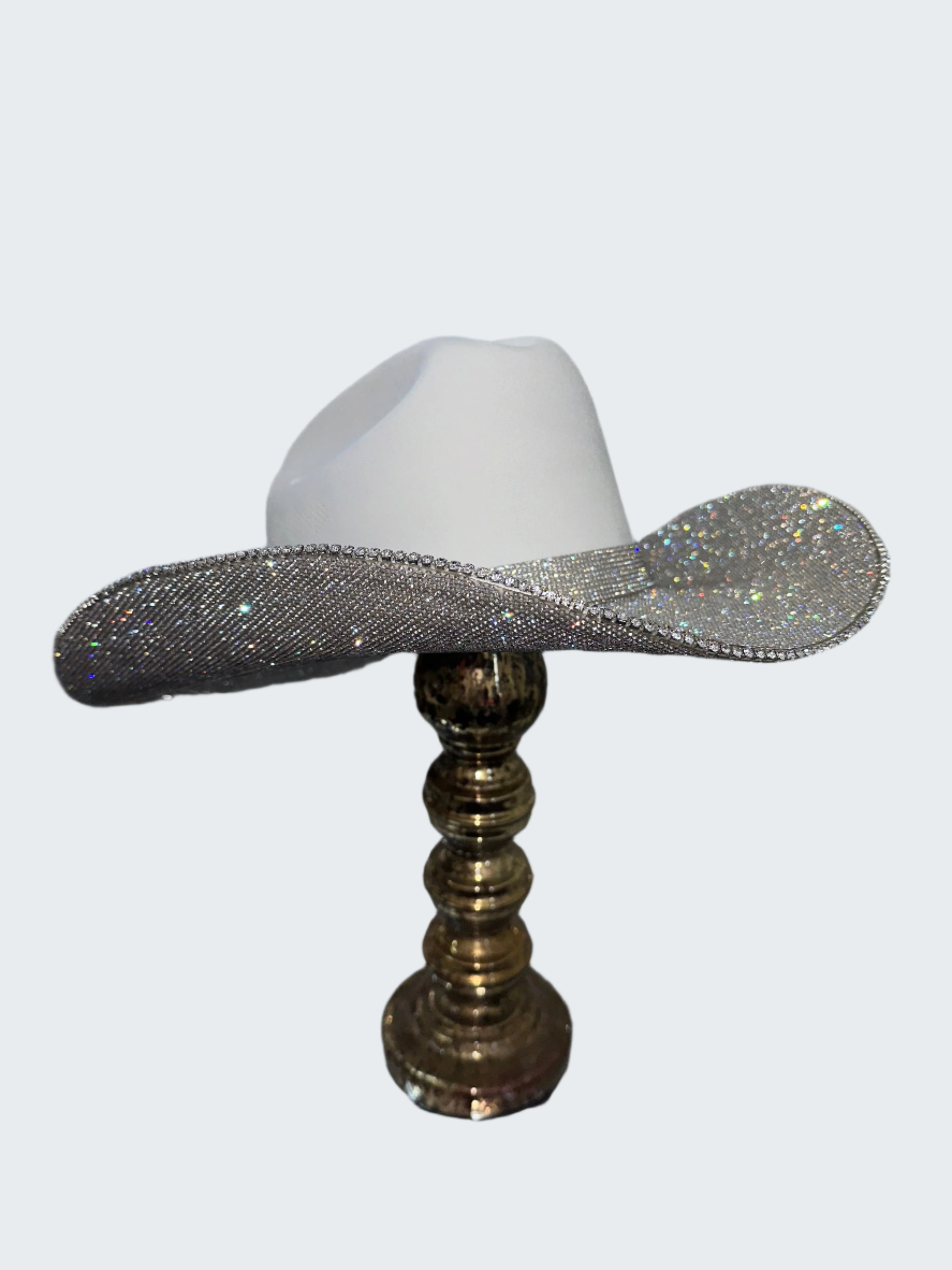 White cowboy hat with a rhinestone brim on a gold stand against a silver sequin background