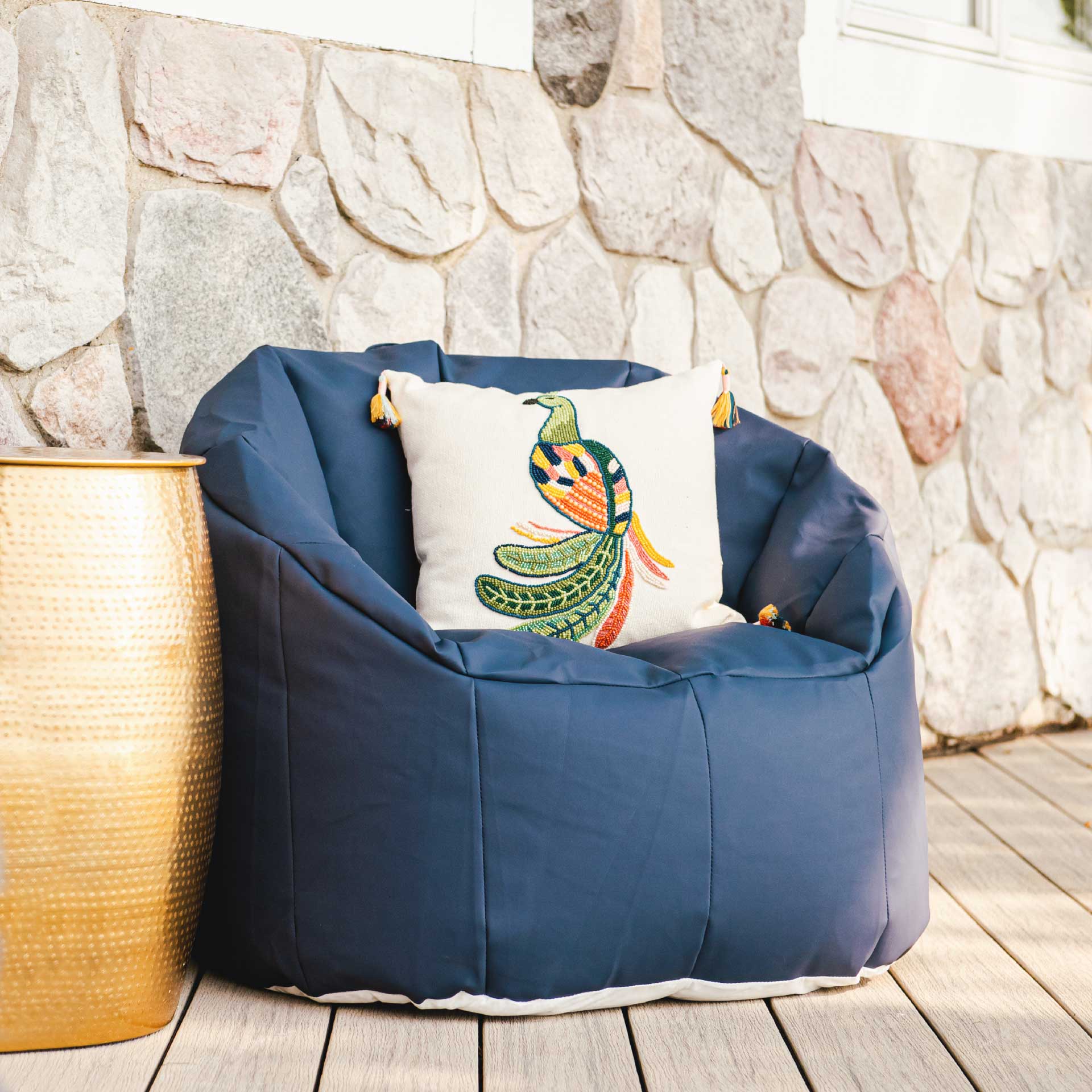 Blue bean bag chair with a colorful pillow against a stone wall.