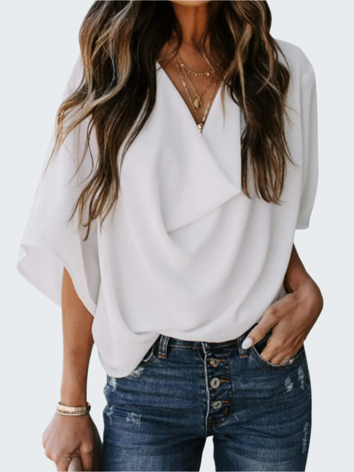A woman wearing a white ruched three-quarter sleeve blouse with a V-neckline, paired with blue jeans.