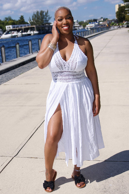 Woman in a white dress standing on a sidewalk by a waterfront.
