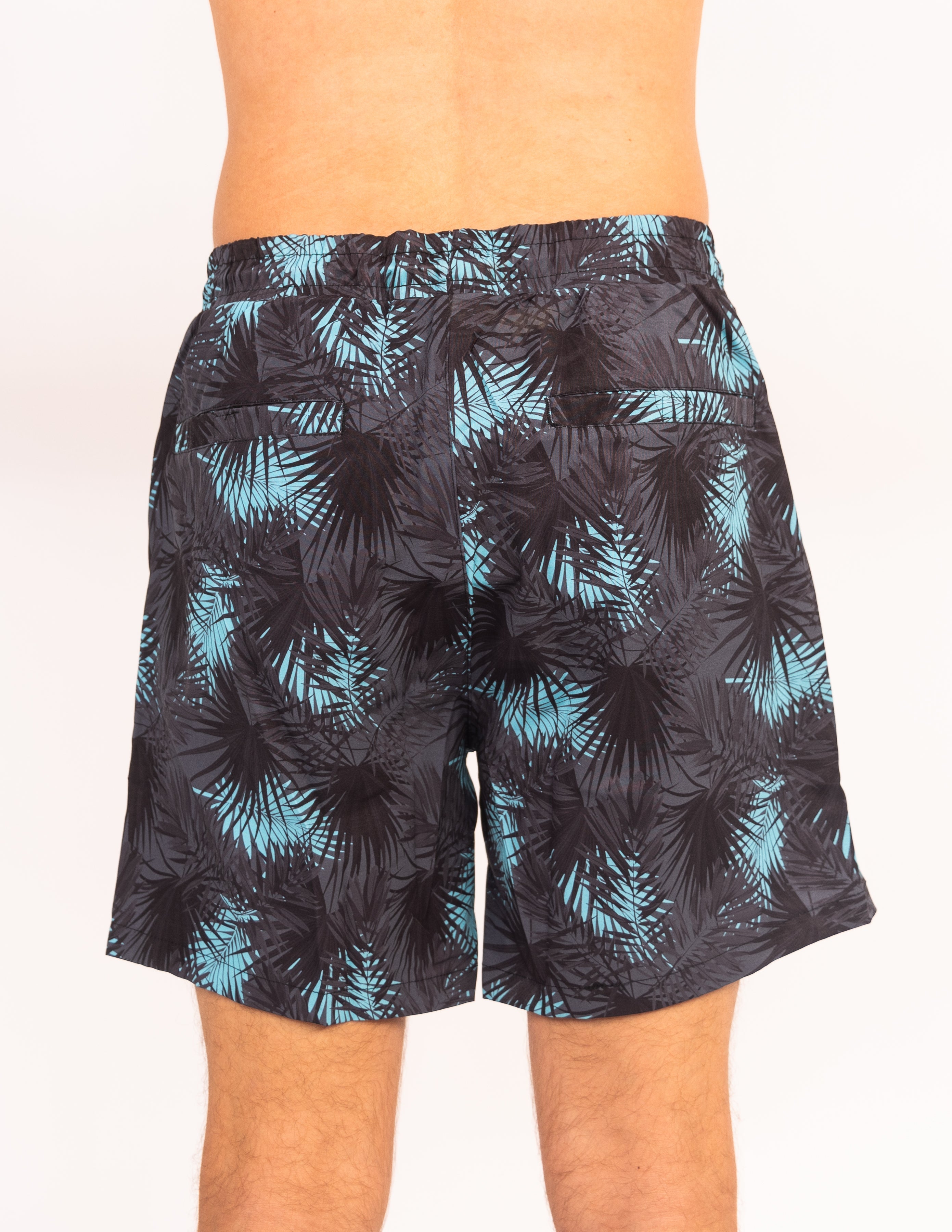 Black swim shorts with blue palm leaf pattern worn by a person on a white background