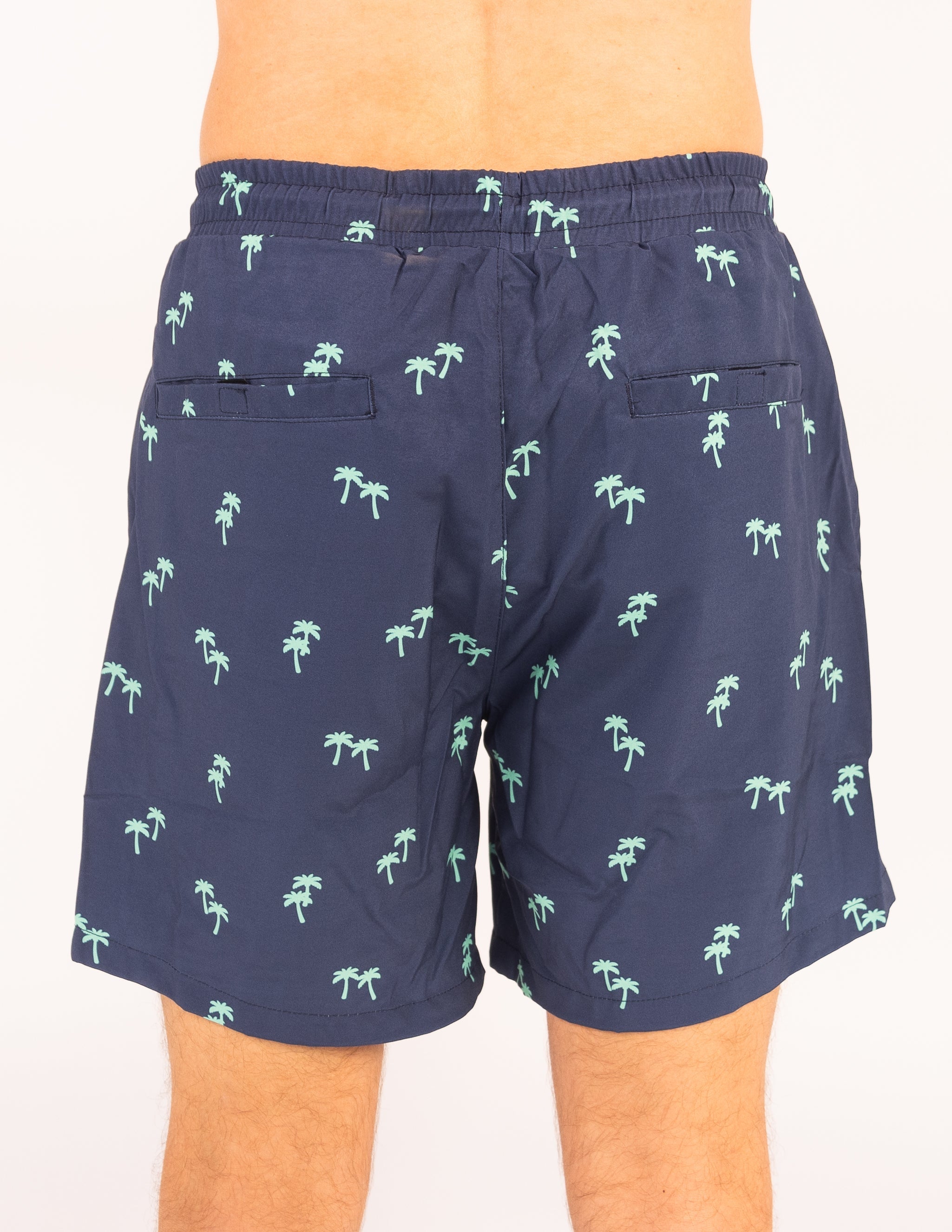 Navy shorts with palm tree pattern worn by a person on a white background
