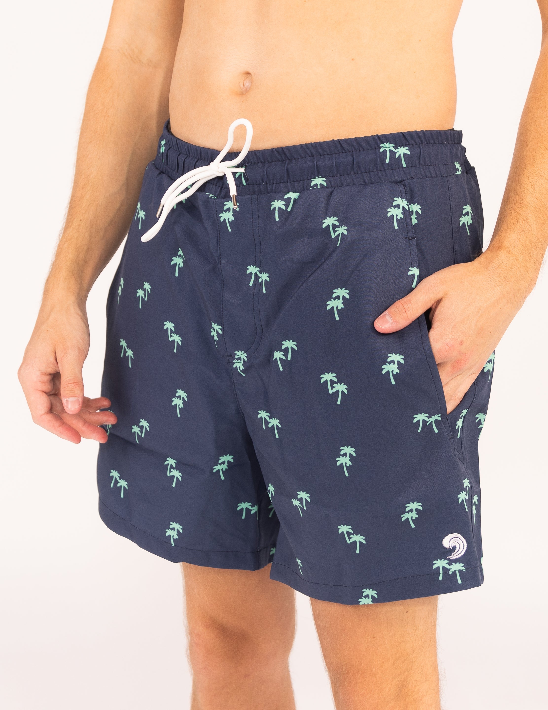 Navy blue swim shorts with palm tree pattern worn by a person on a white background
