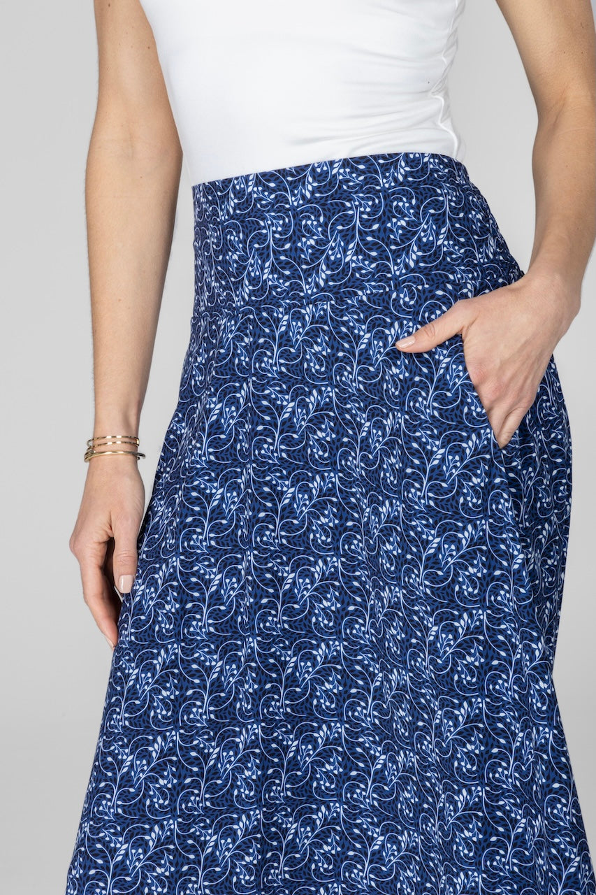 Person wearing a blue patterned skirt with a white top on a plain background