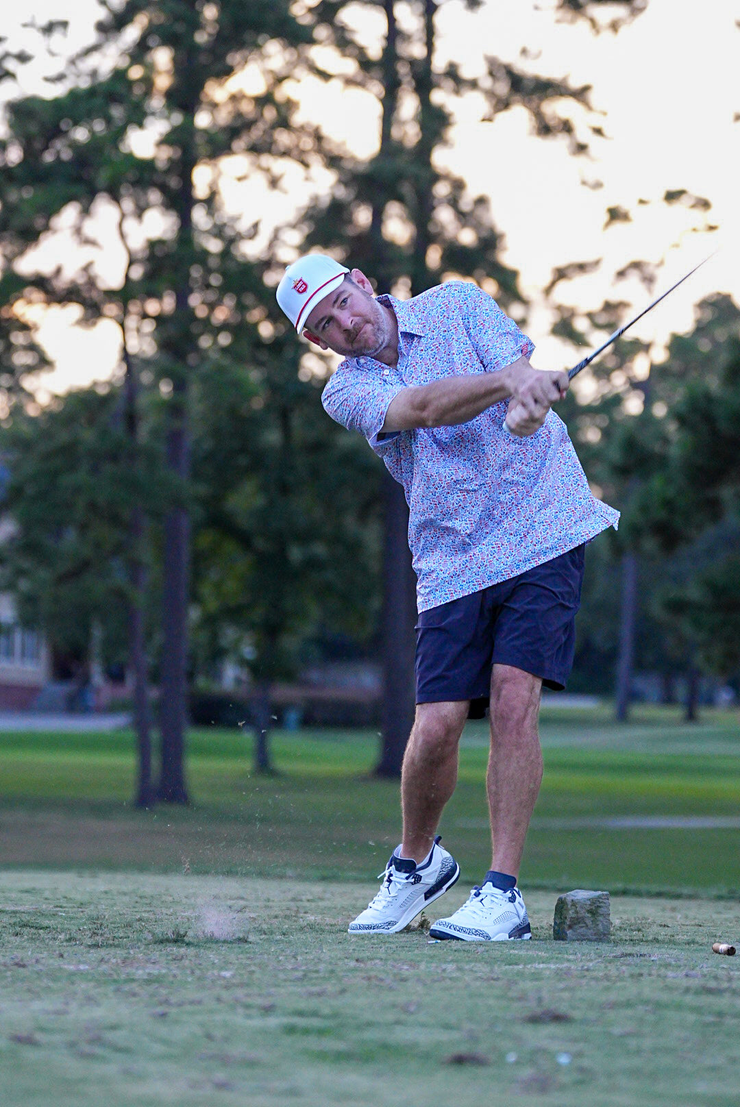 Man playing golf on a green course with trees in the background