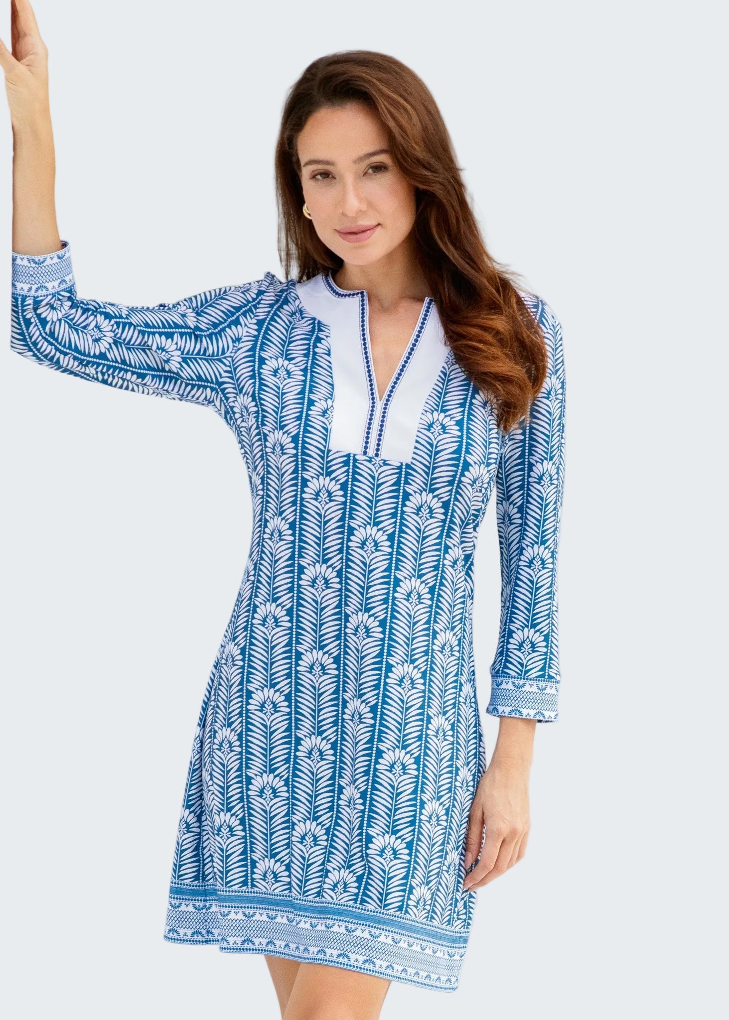 Woman wearing a blue and white patterned dress standing in front of a white wall.