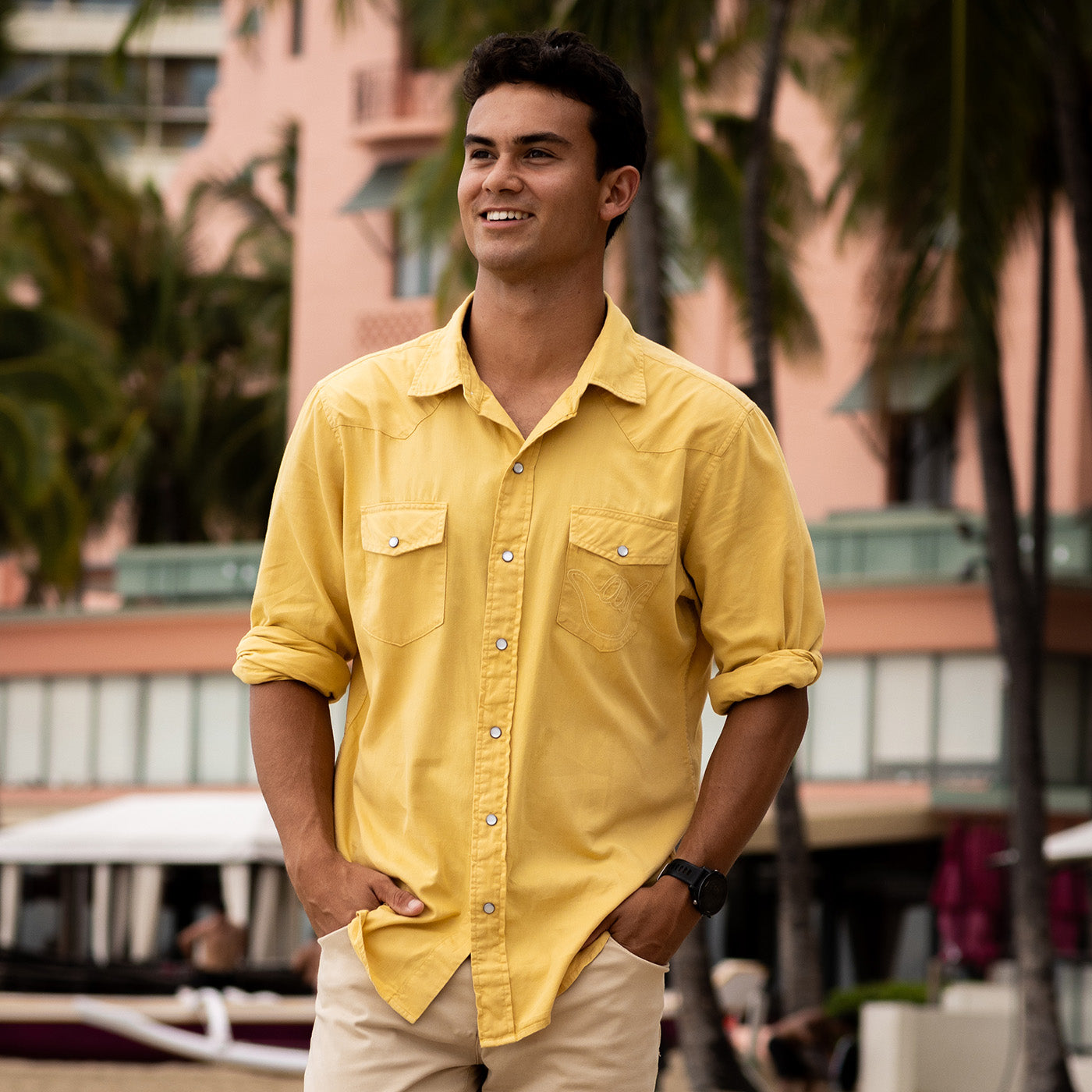 Man wearing a yellow shirt standing outdoors with blurred background