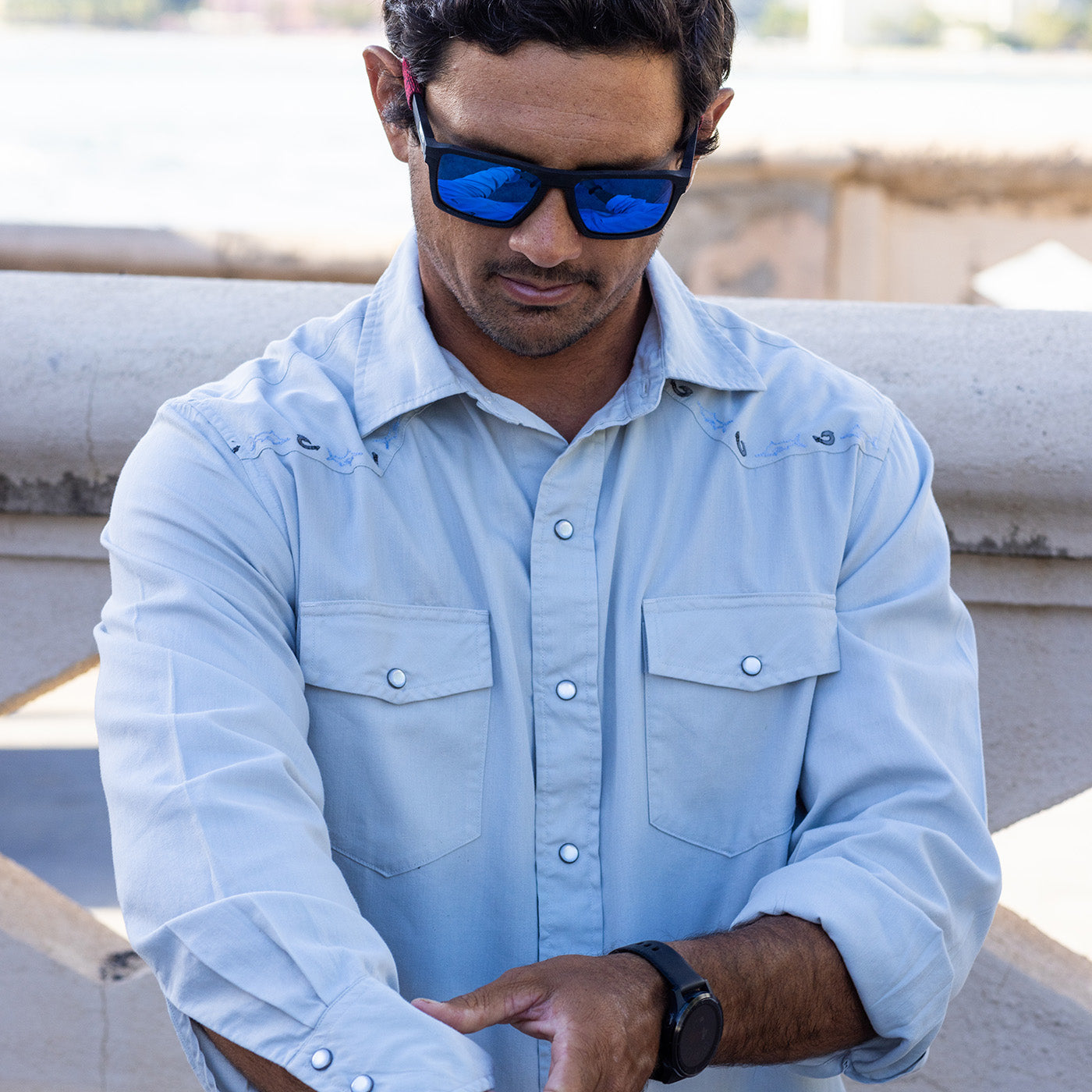 Man wearing a light blue shirt and sunglasses sitting on a bench.