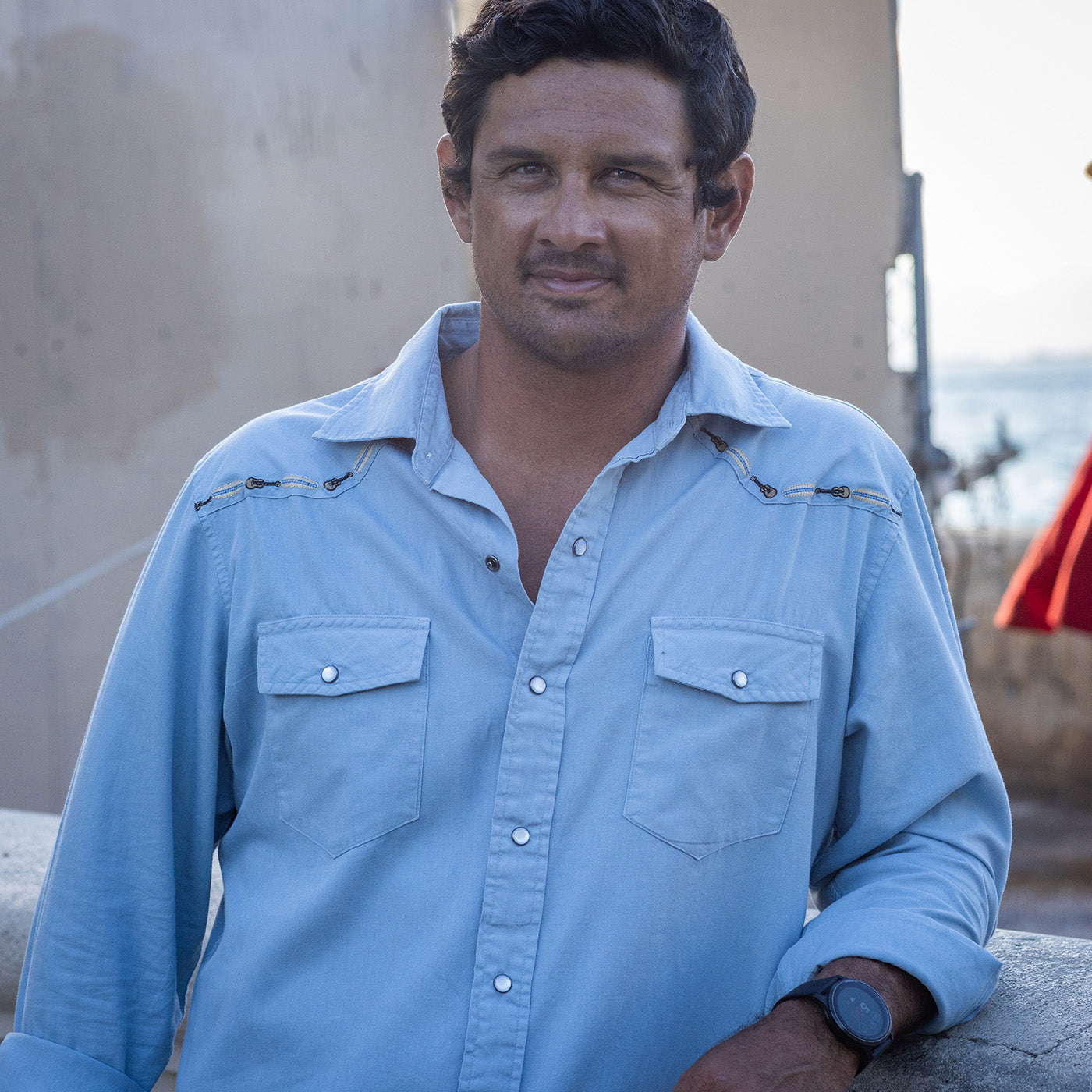 Man wearing a light blue shirt standing outdoors with a neutral background