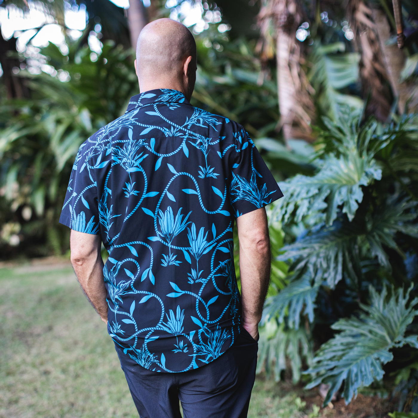 Man wearing a blue and black patterned shirt standing in a garden