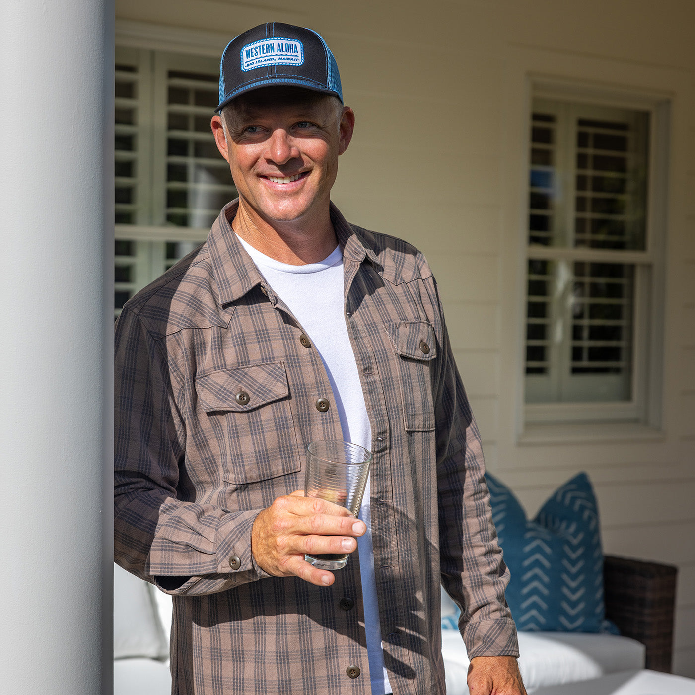 Man wearing a cap and plaid jacket holding a glass outdoors.