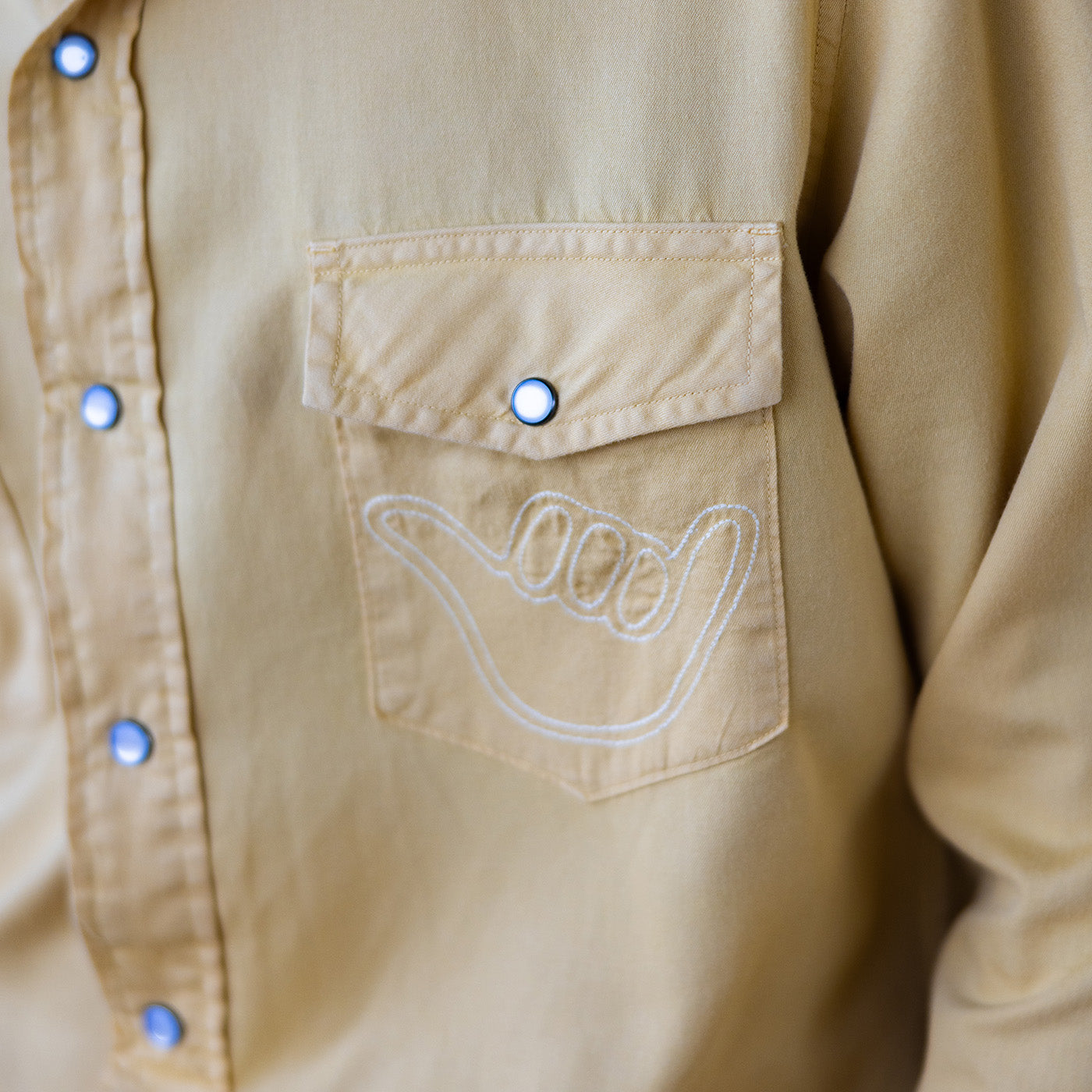 Beige shirt with a pocket and embroidered design on a neutral background