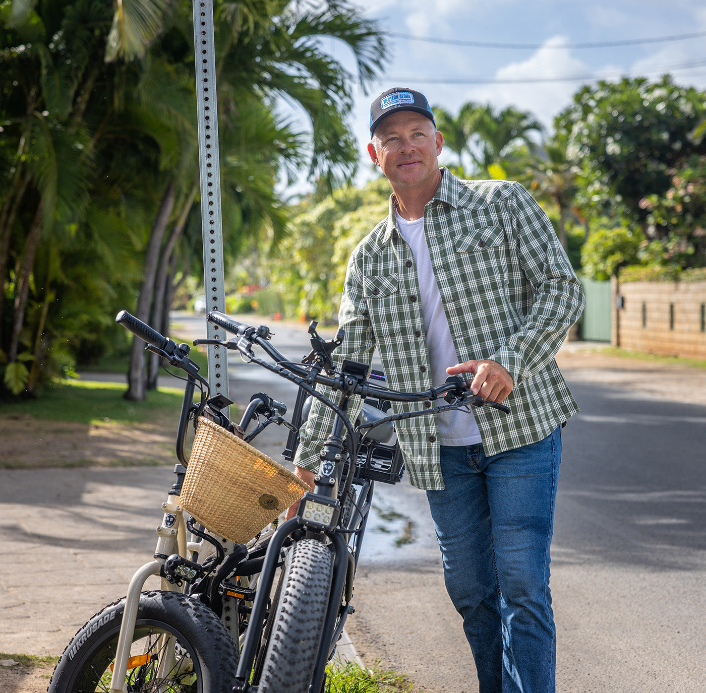 Man standing next to a bicycle with a basket on a street with greenery in the background