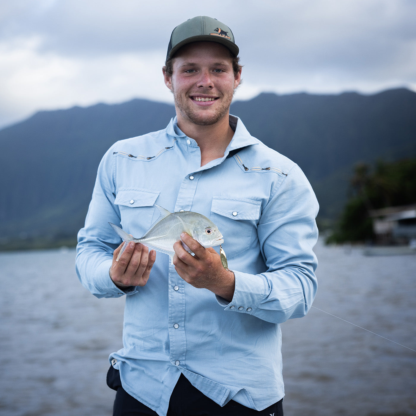 Man holding a fish with mountains in the background