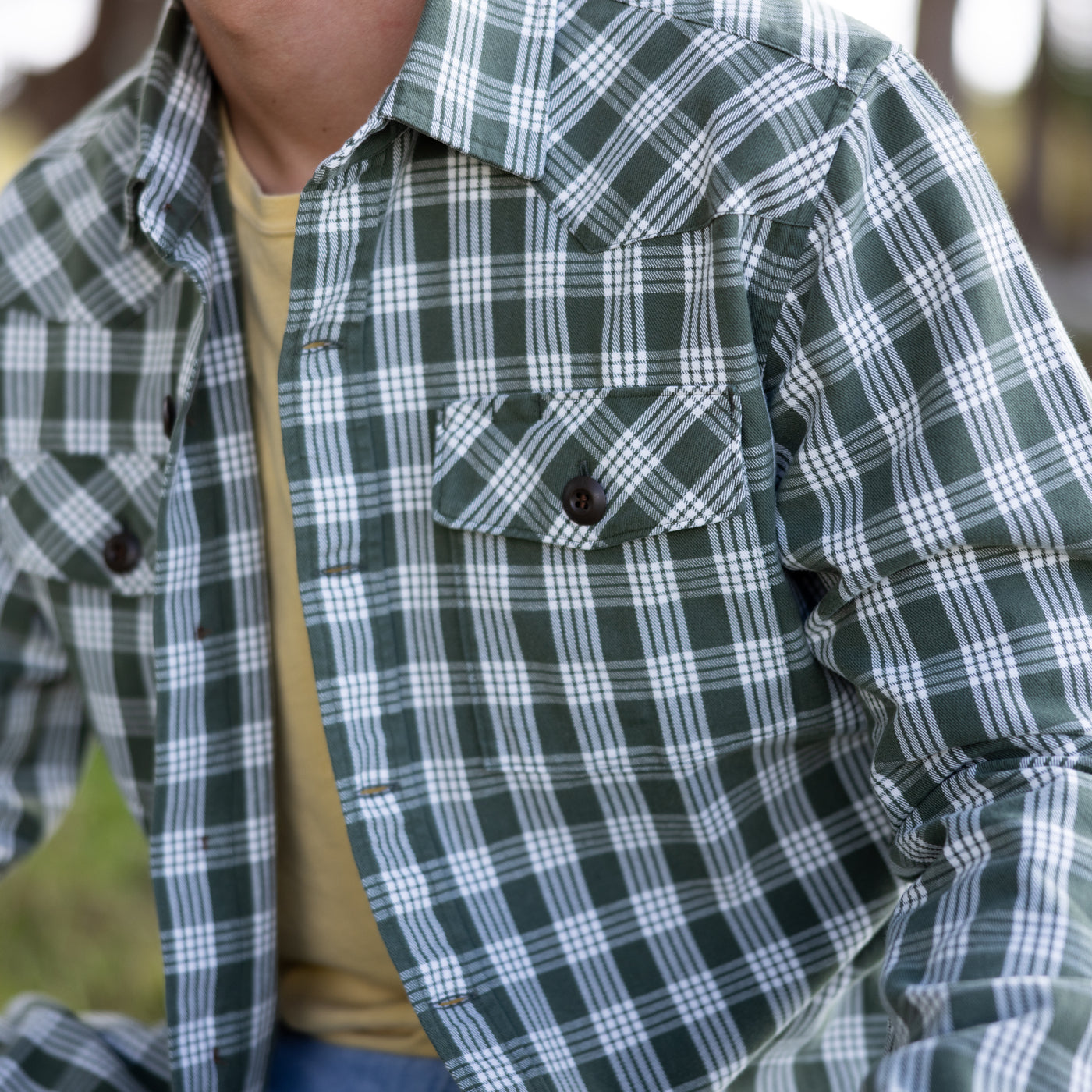 Green and white plaid shirt worn by a person with a blurred natural background