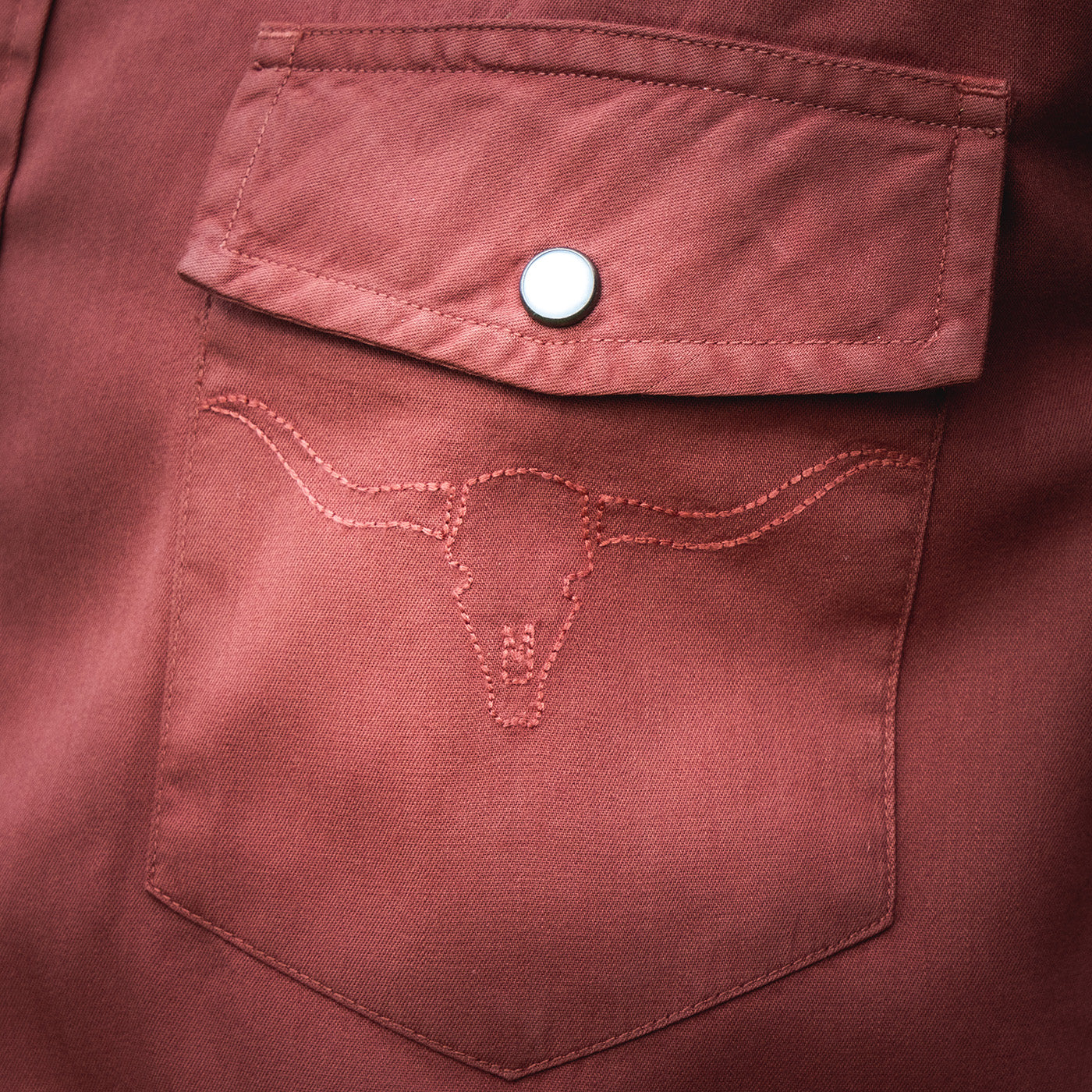 Close-up of a maroon pocket with stitching detail on a garment.