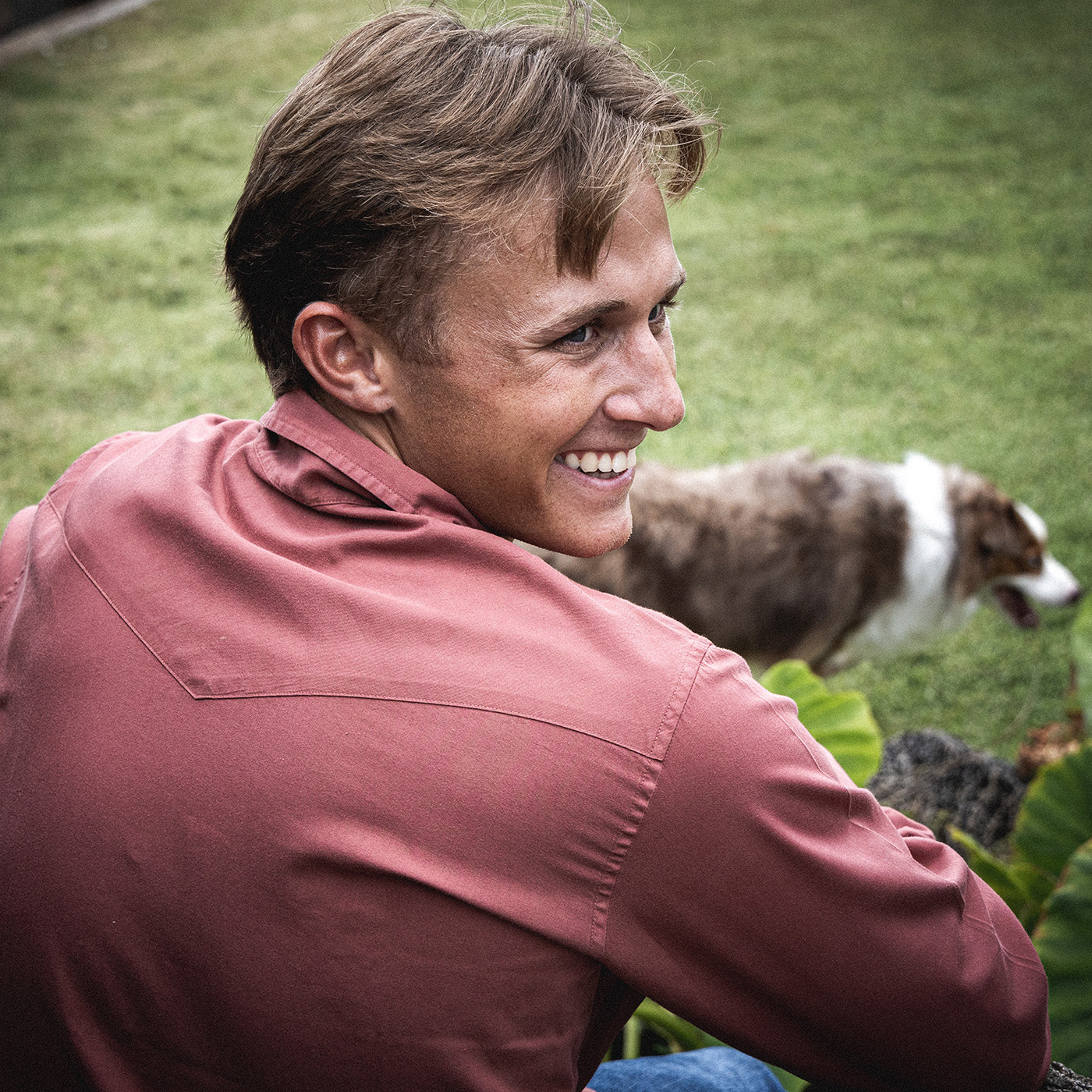 Man sitting outdoors with a dog in the background