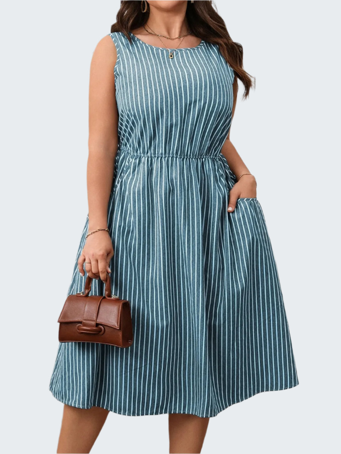 A model wearing a plus size striped round neck sleeveless dress in blue and white, with a brown belt, holding a brown bag.