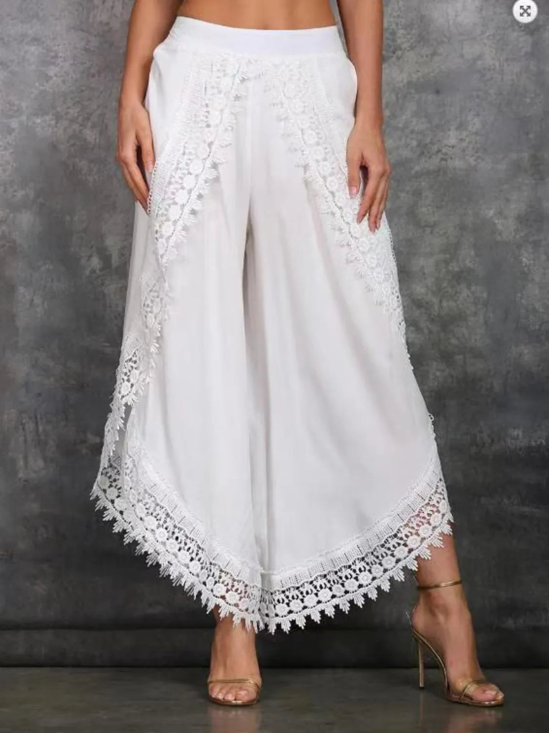 White wide leg pants with lace detailing at the hem, shown on a model wearing high heels.