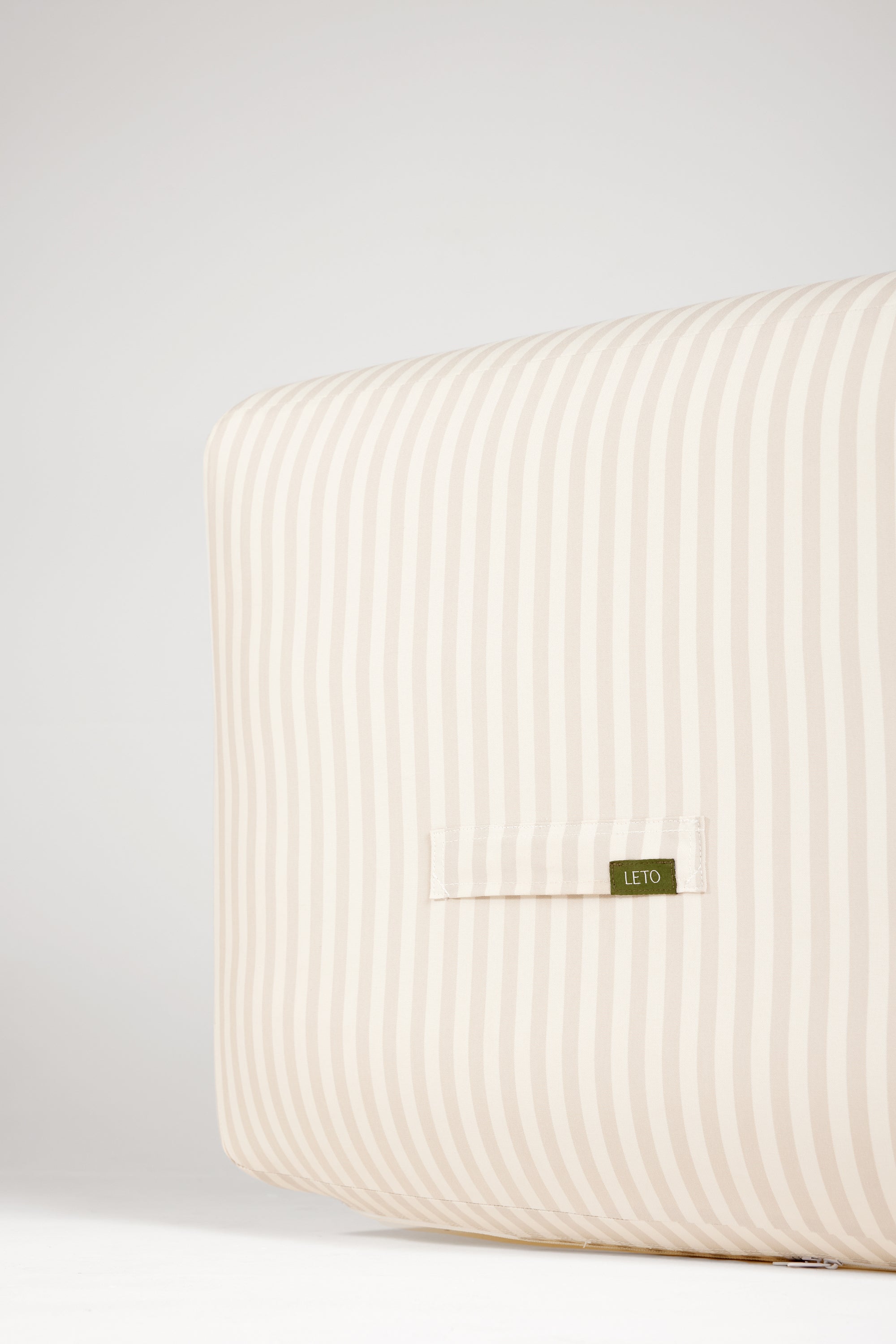 Beige striped pillow with a brand label on a light gray background
