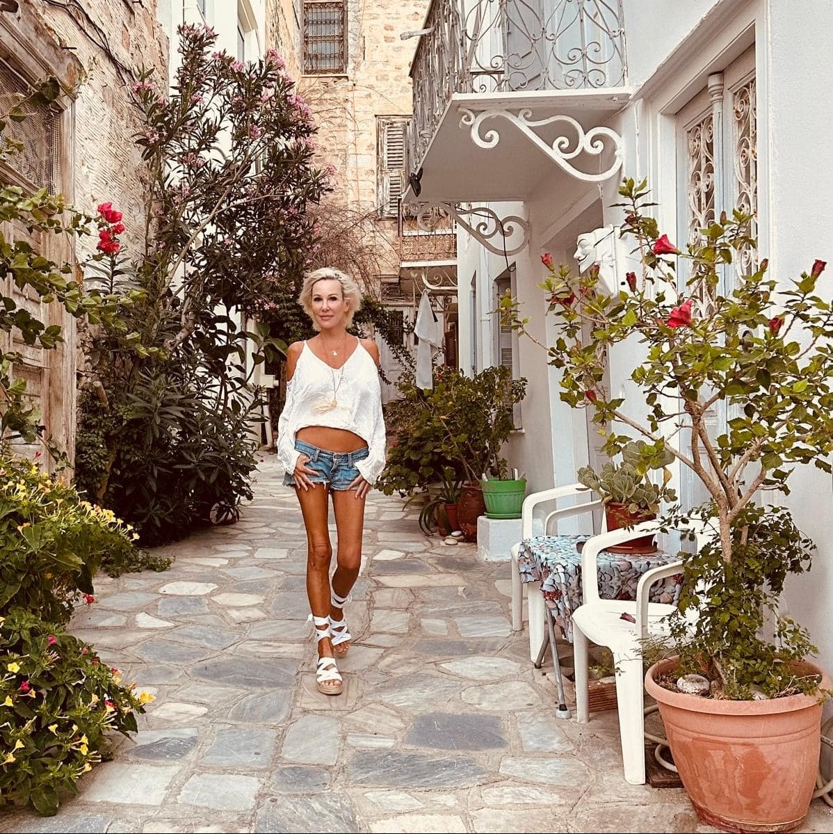 Woman walking down a narrow street lined with plants and buildings
