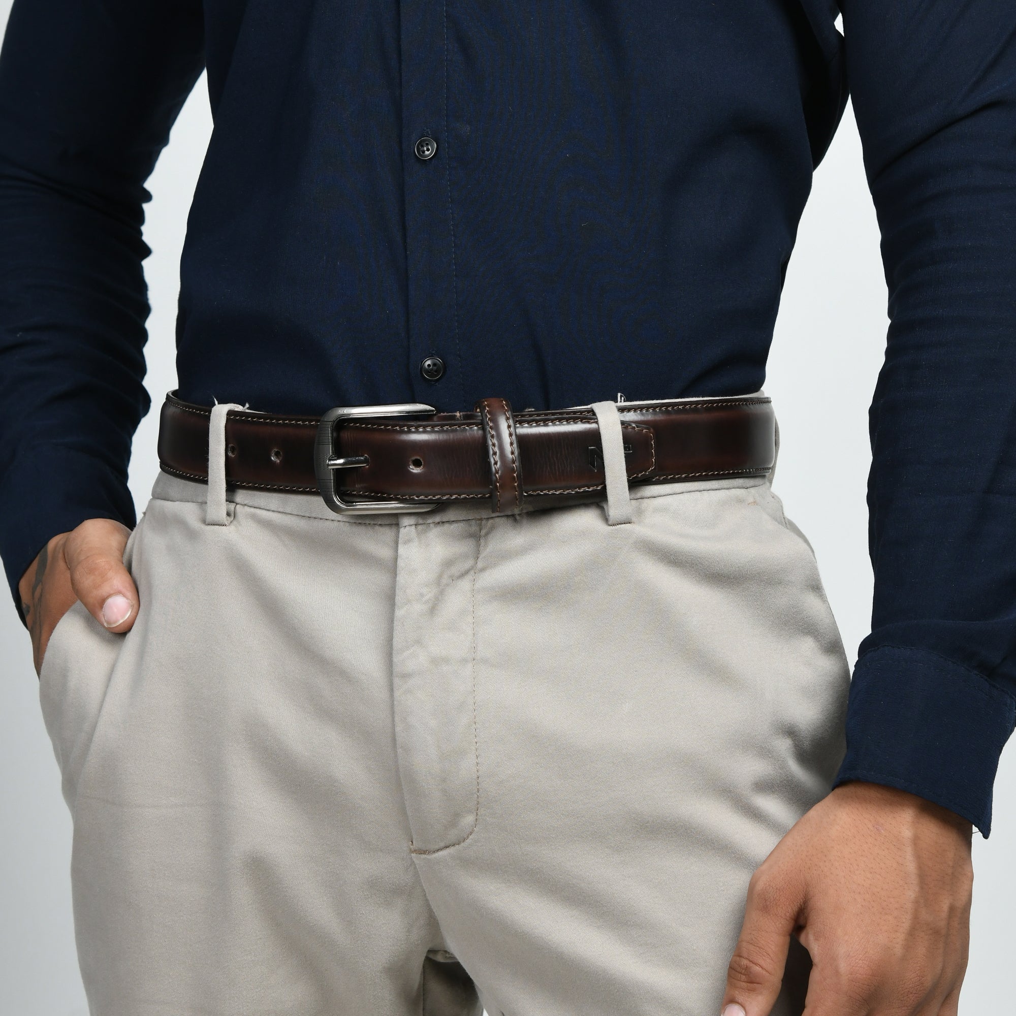 Person wearing a navy shirt, beige pants, and a brown belt on a light gray background