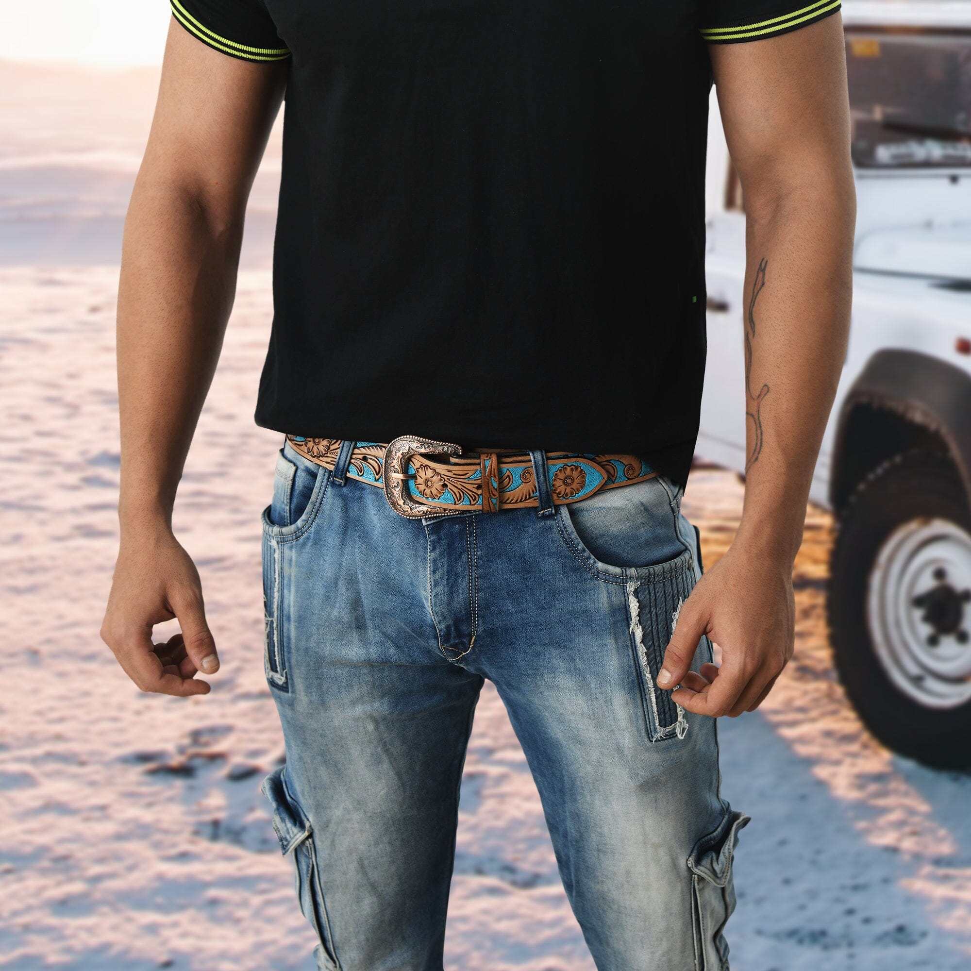 Person wearing a black shirt, blue jeans, and a decorative belt with a blurred background