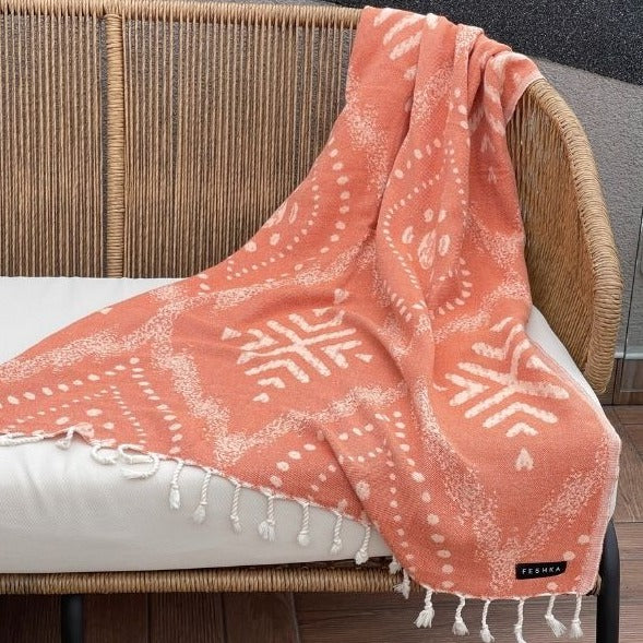 Coral patterned towel draped over a wicker chair with a blurred background
