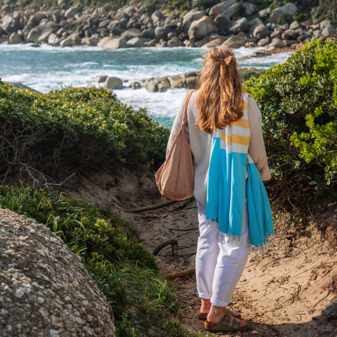 Woman walking along a coastal path with ocean and rocks in the background